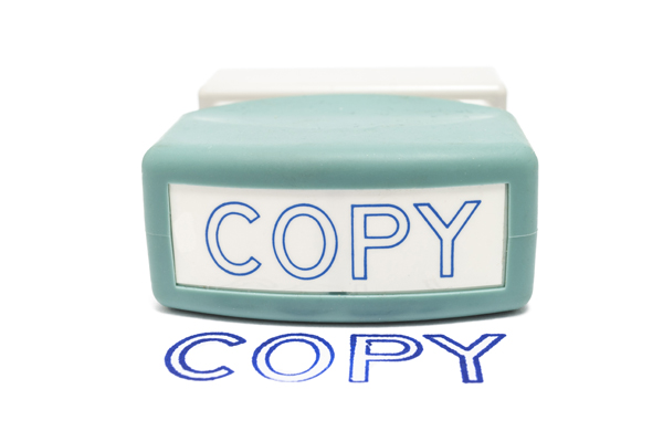 Self-inking rubber Copy stamp next to the word "COPY" stamped on paper, isolated on white.