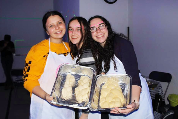 Three women holding pans of challah dough